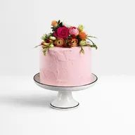 A pink cake with flowers on top of it on a white cake stand.