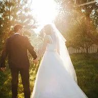 A bride and groom are walking through a field holding hands.