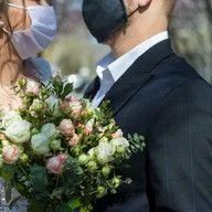 A bride and groom wearing face masks and holding a bouquet of flowers.