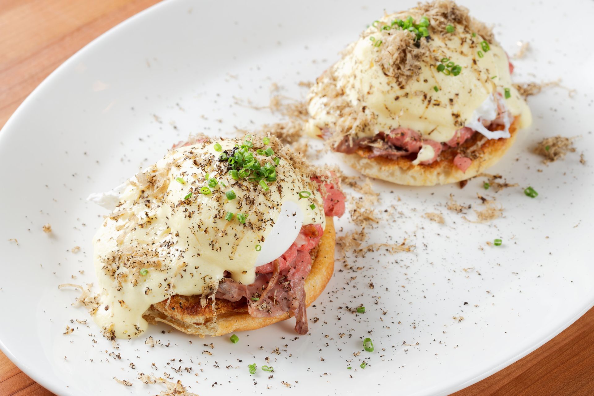 Two sandwiches are on a white plate on a wooden table.