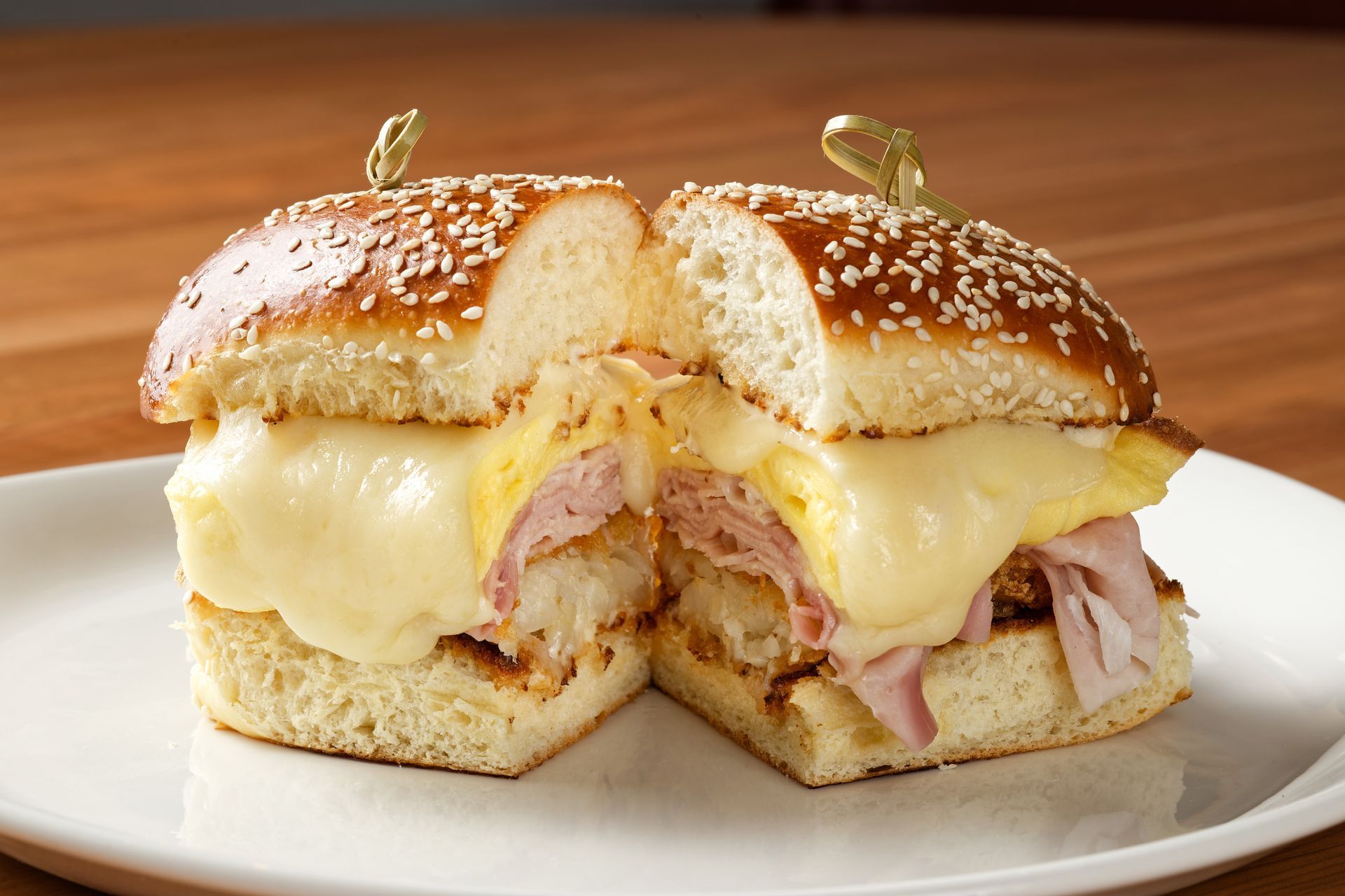 A ham and cheese sandwich is cut in half on a white plate.