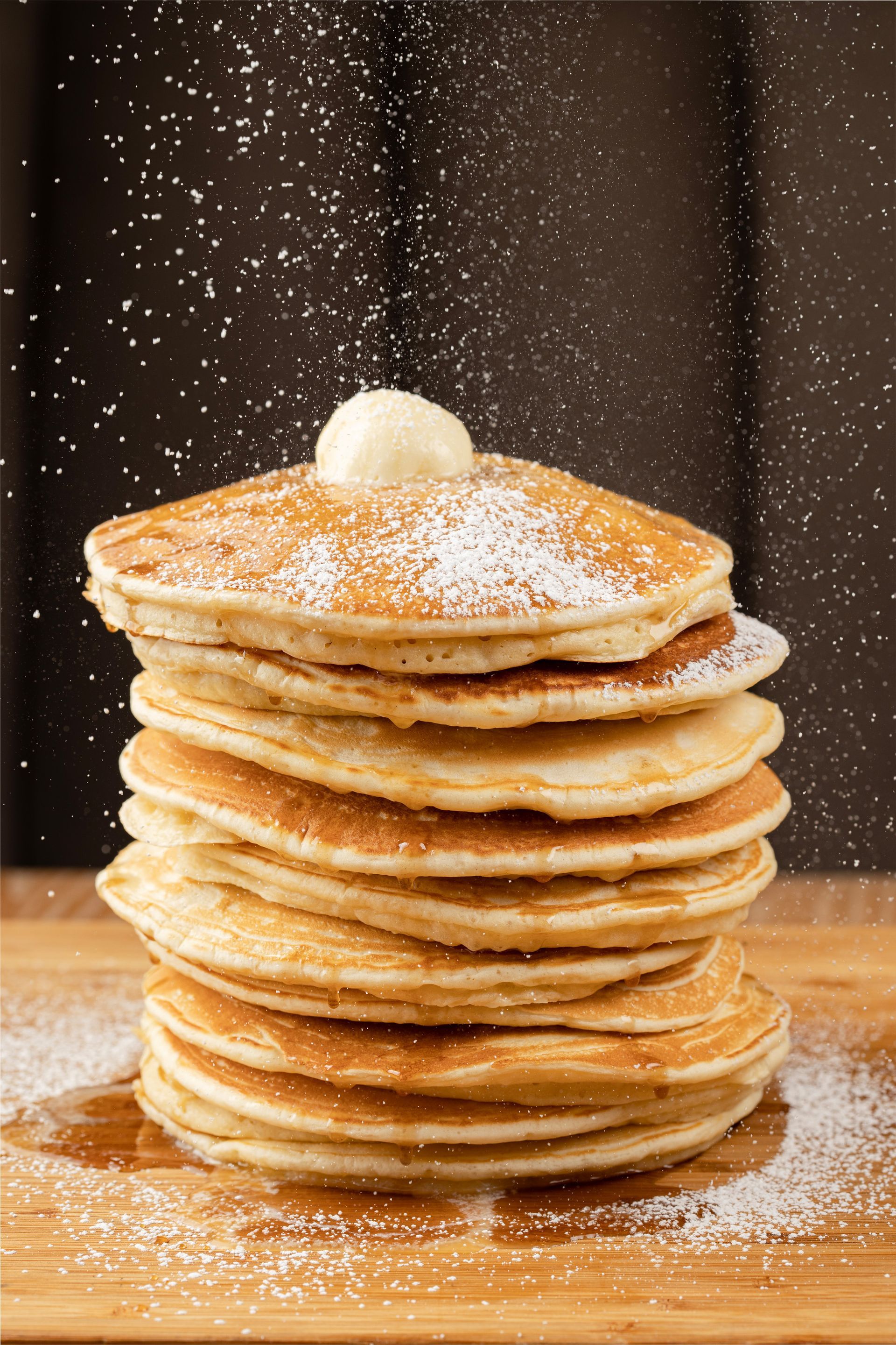 A stack of pancakes with butter and powdered sugar on top.