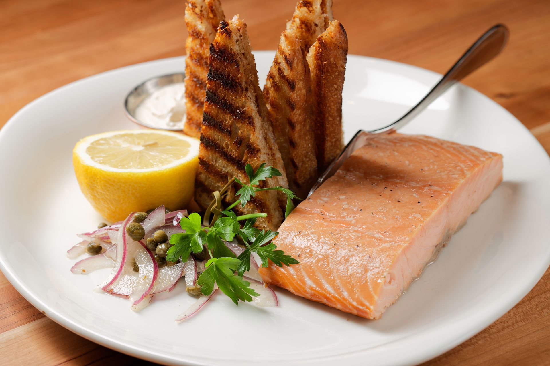 A white plate topped with a piece of salmon and a slice of lemon.