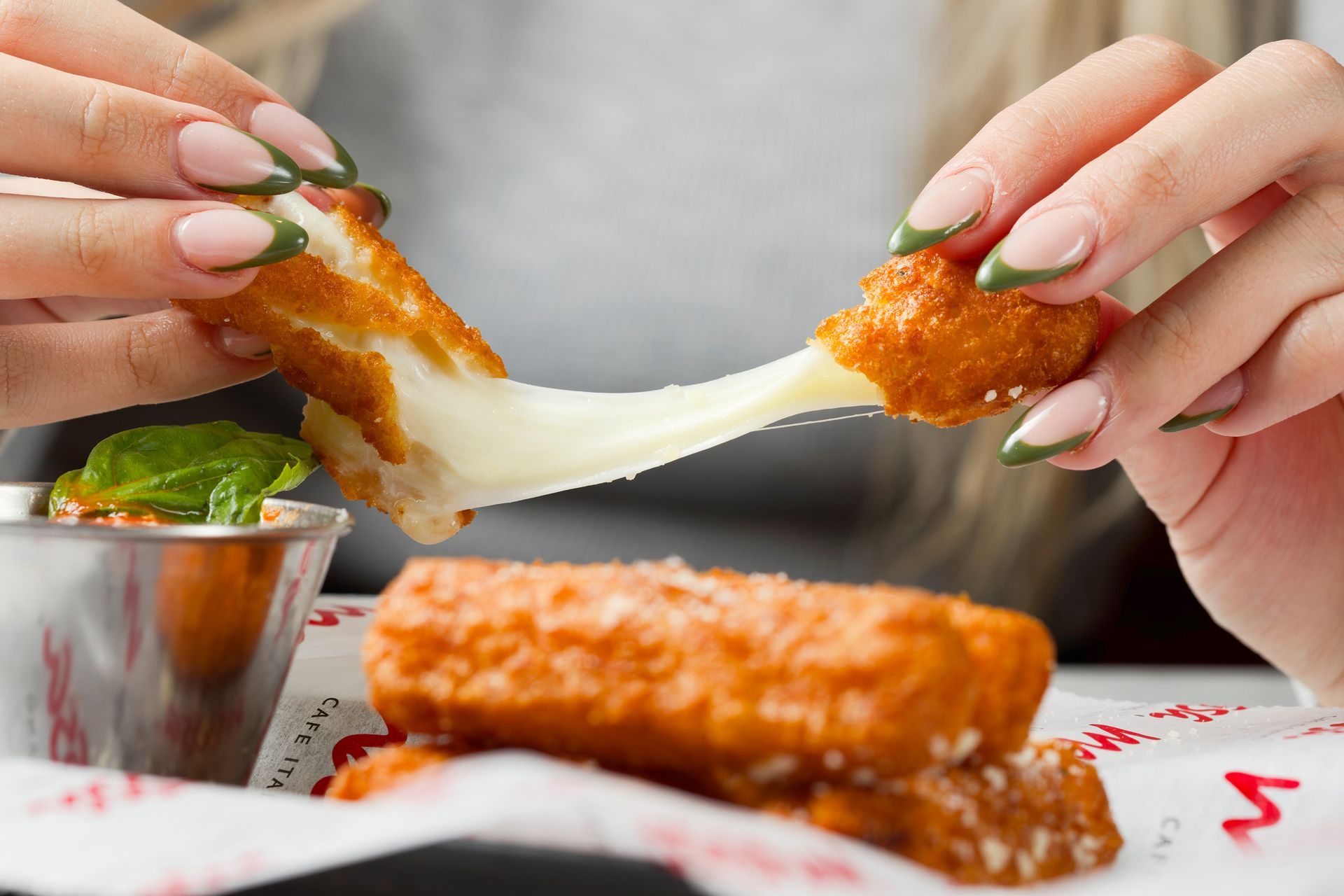 A person is holding a piece of food with cheese sticking out of it.