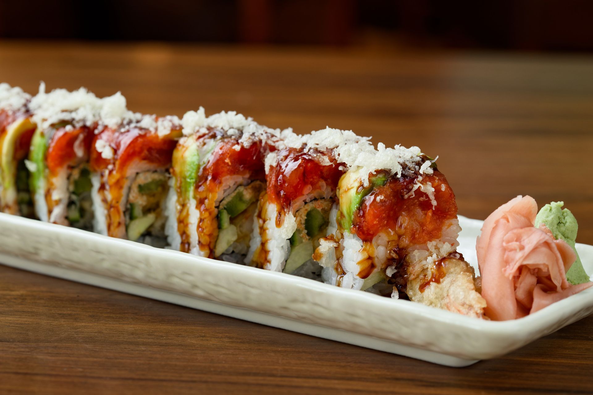 A row of sushi rolls on a white plate on a wooden table.