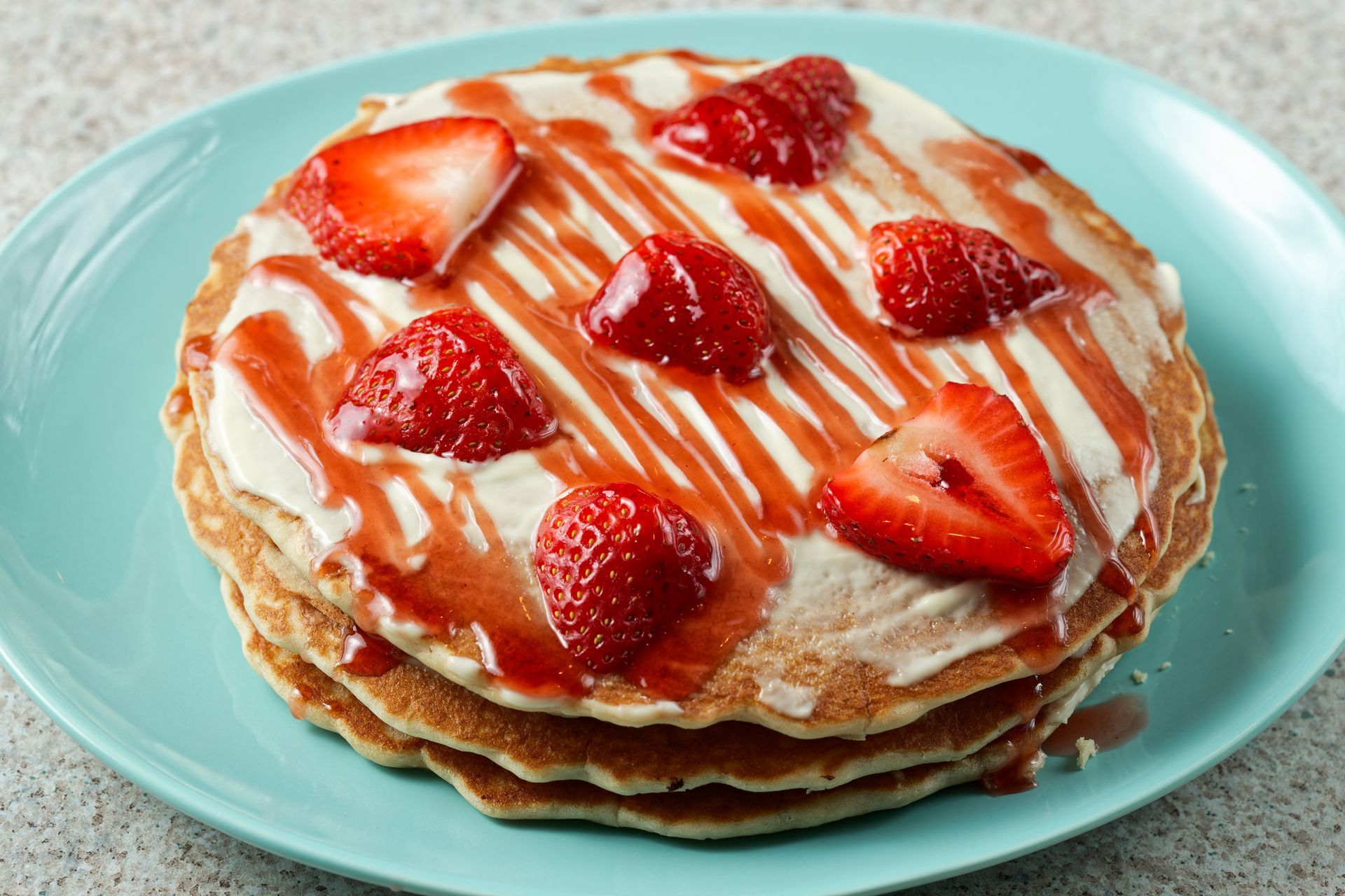 A stack of pancakes with strawberries on top on a blue plate