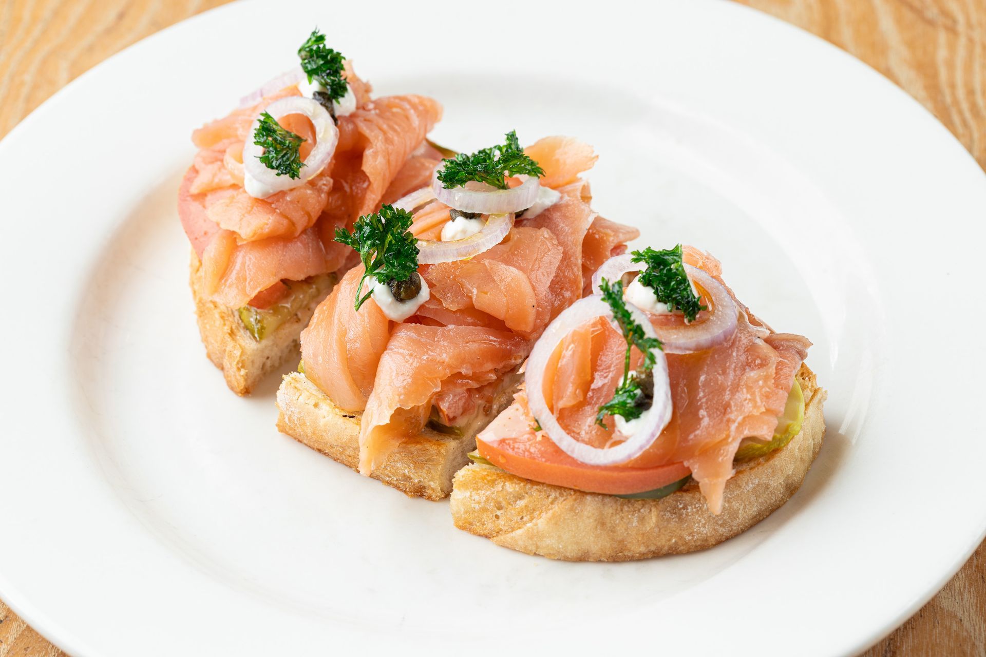 A white plate topped with three sandwiches with smoked salmon and onions.