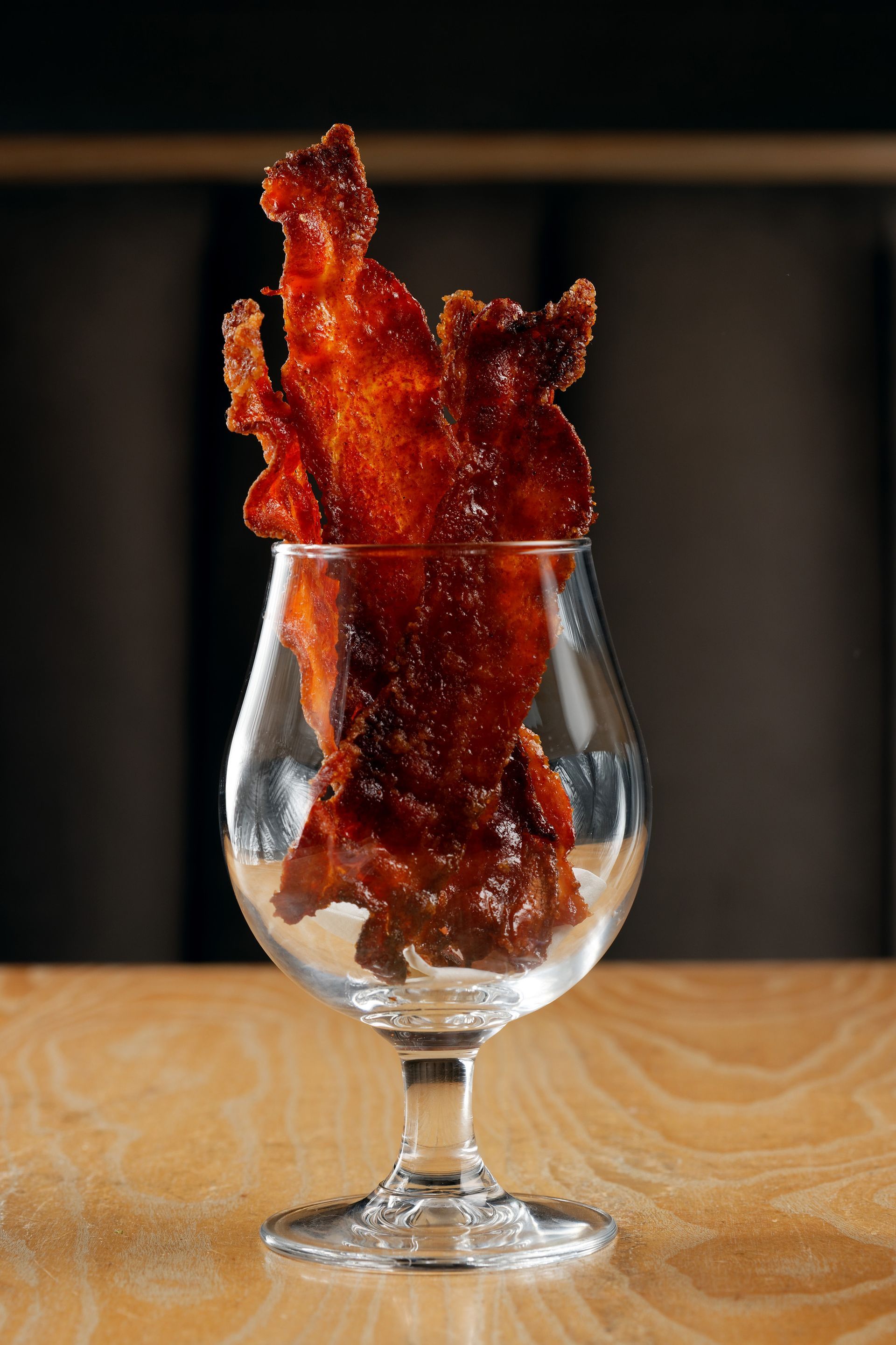 A glass filled with bacon is sitting on a wooden table.