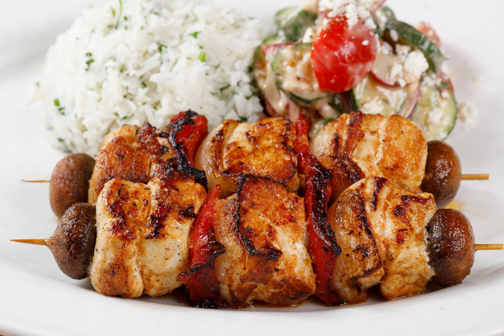 A white plate topped with chicken skewers , rice and a salad.