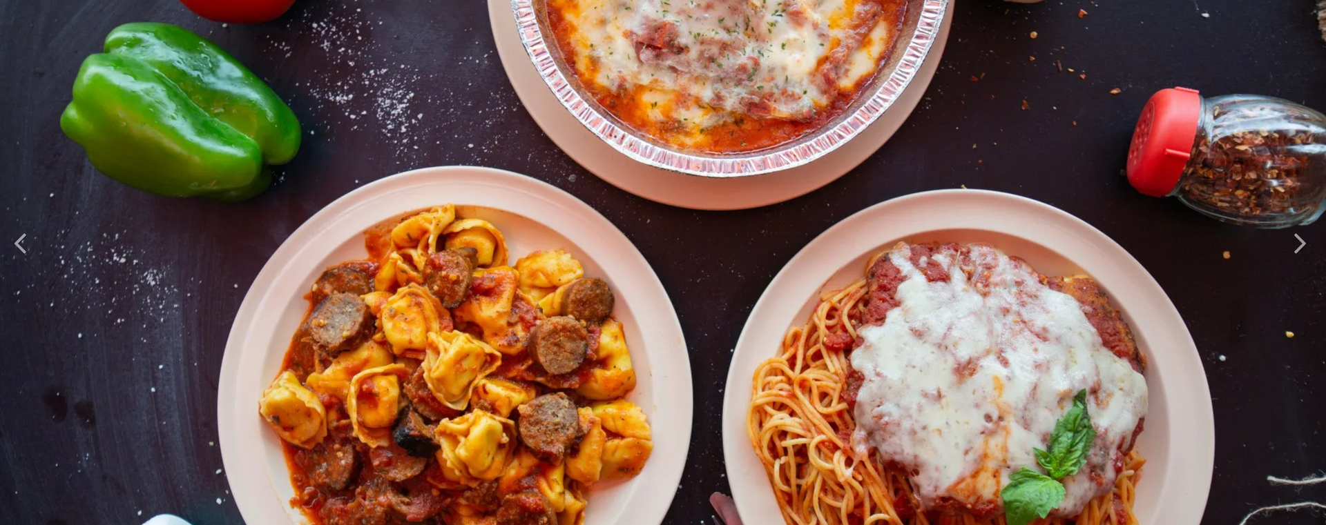 Three plates of pasta and a pizza on a table.
