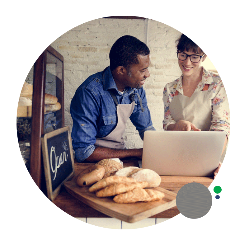 A man and a woman are looking at a laptop in a bakery