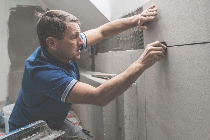 Worker applying plaster to a wall in a construction site, smoothing a gray concrete surface.