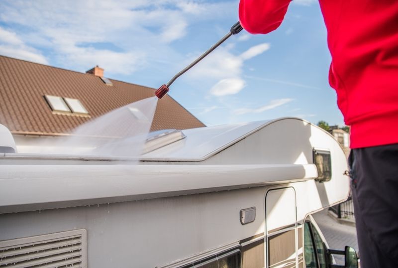 A man is cleaning the roof of a camper with a high pressure washer.