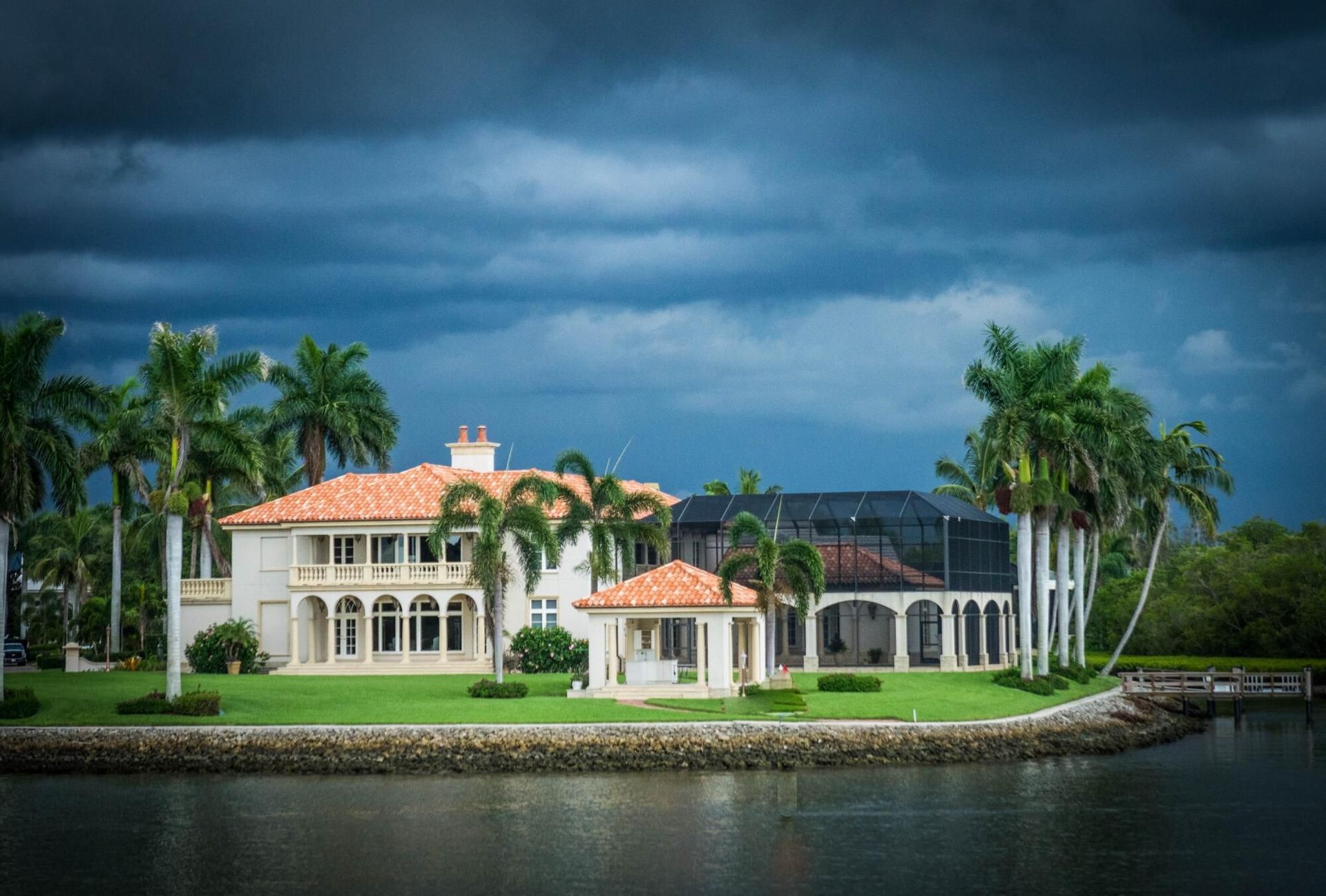 A large house is sitting on a small island in the middle of a body of water.