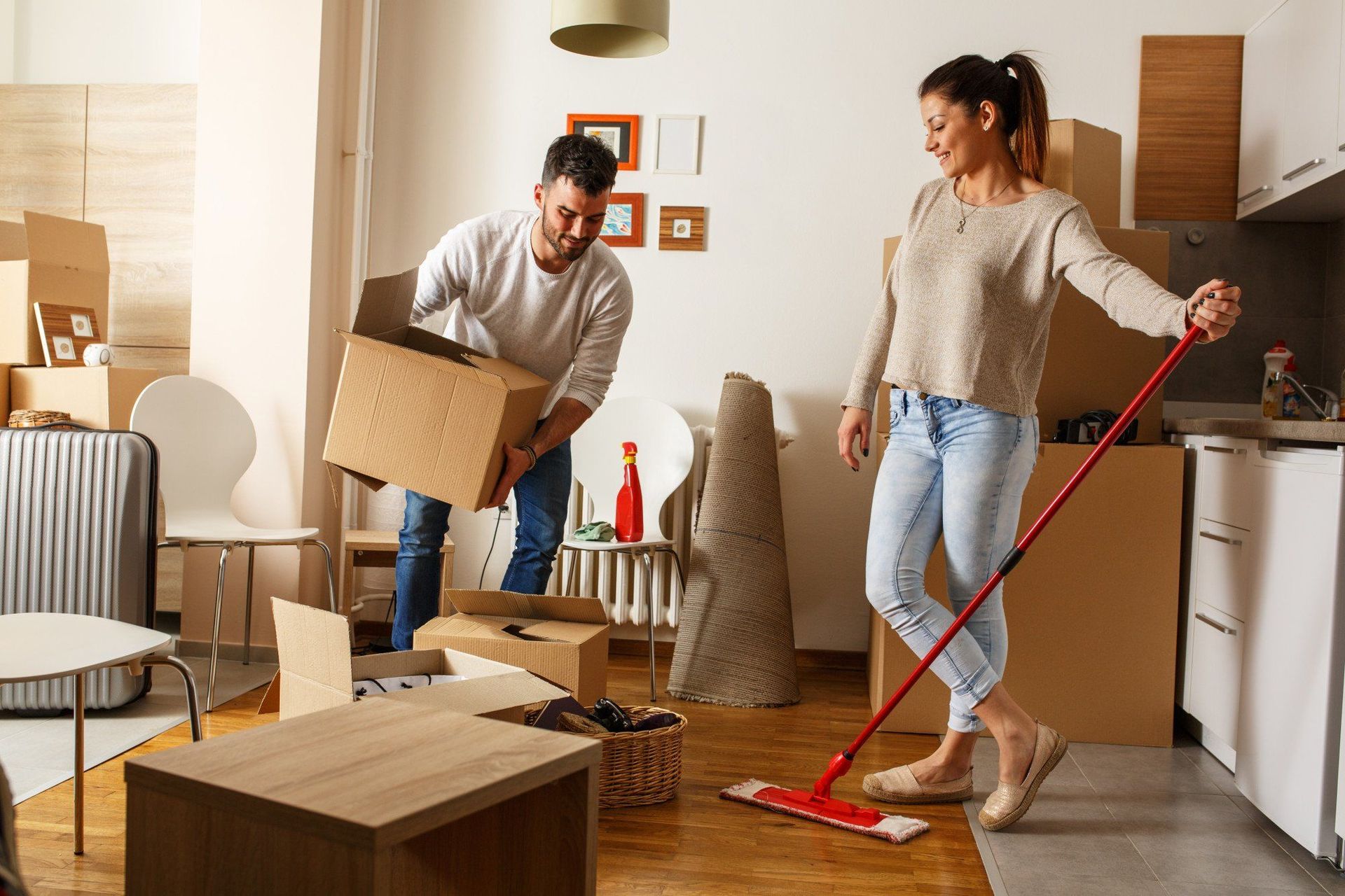 A man is carrying a box and a woman is mopping the floor.