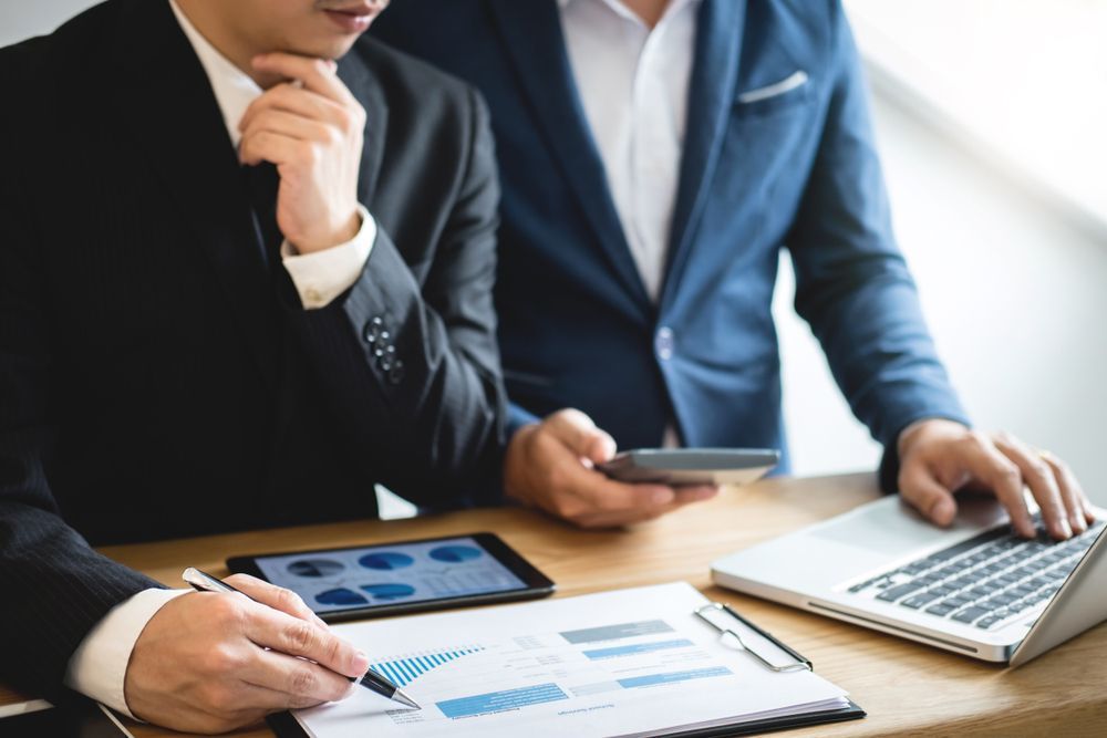 Two businesspeople analyzing charts and data on a tablet, laptop, and paper, discussing strategy. GMS Legal & Conveyancing In 38 Canton Beach Rd, Toukley