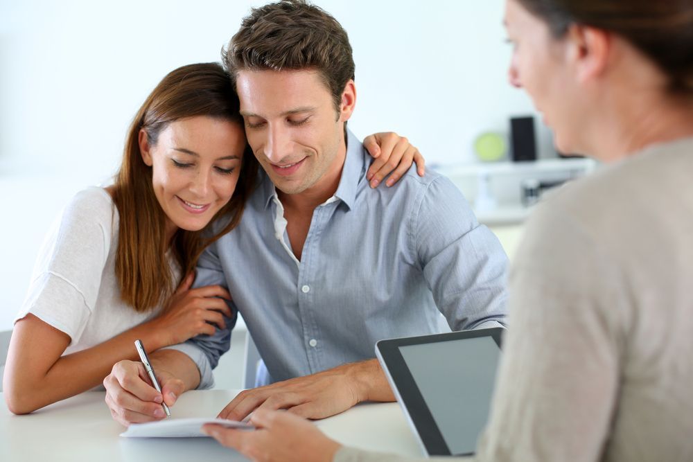 Couple signing a document with a financial adviser at a desk in a bright office— GMS Legal & Conveyancing In 38 Canton Beach Rd Toukley, NSW