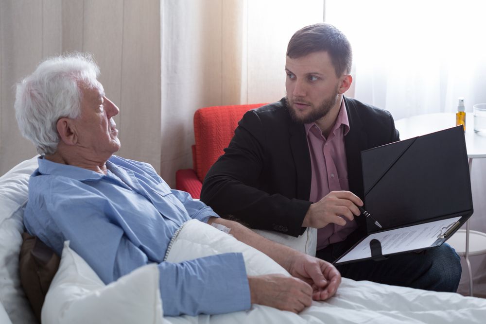Man in suit shows paperwork to older man lying in bed.  GMS Legal & Conveyancing In 38 Canton Beach Rd, Toukley
