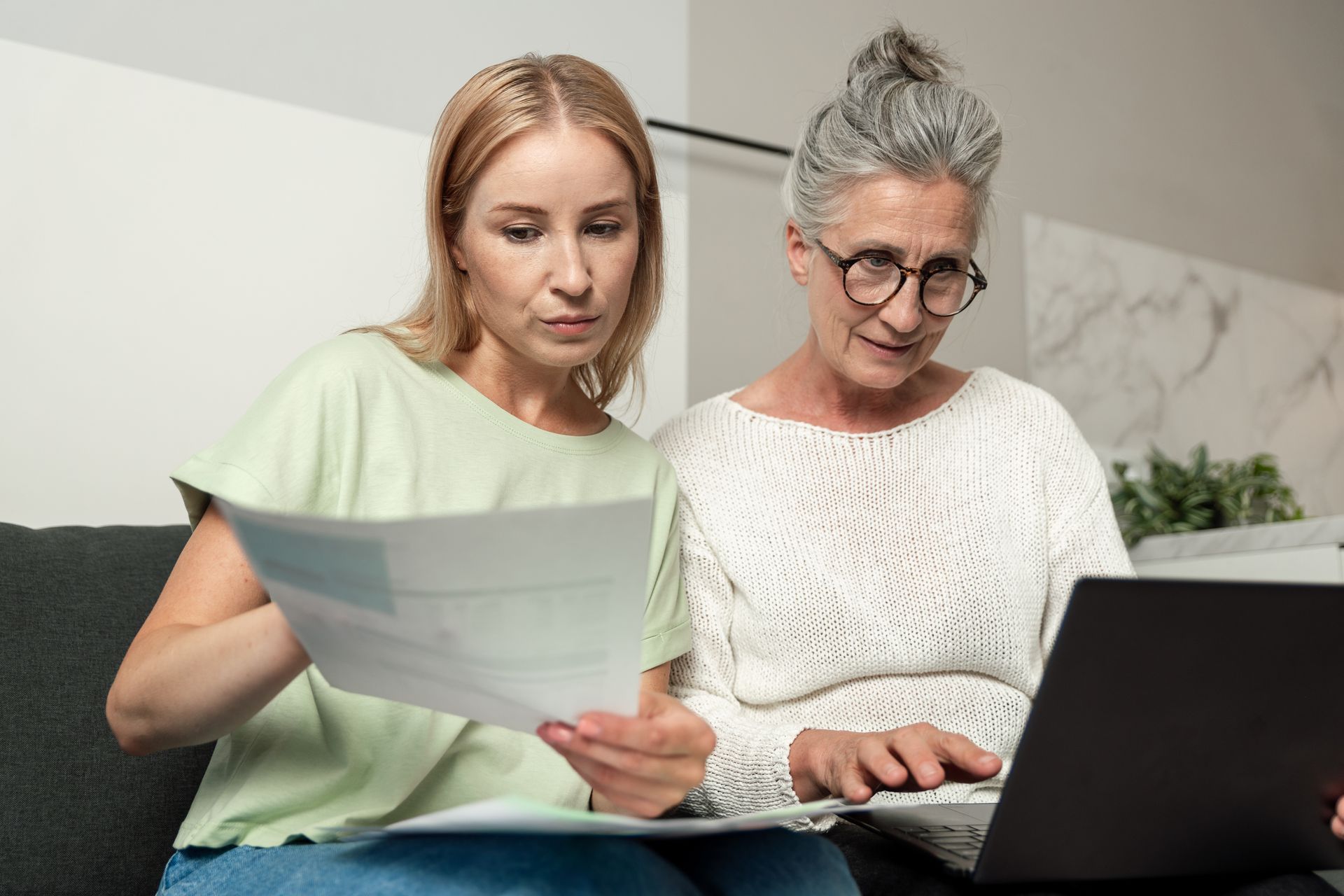 Two people reviewing papers together beside a laptop on a couch — GMS Legal & Conveyancing In 38 Canton Beach Rd, Toukley