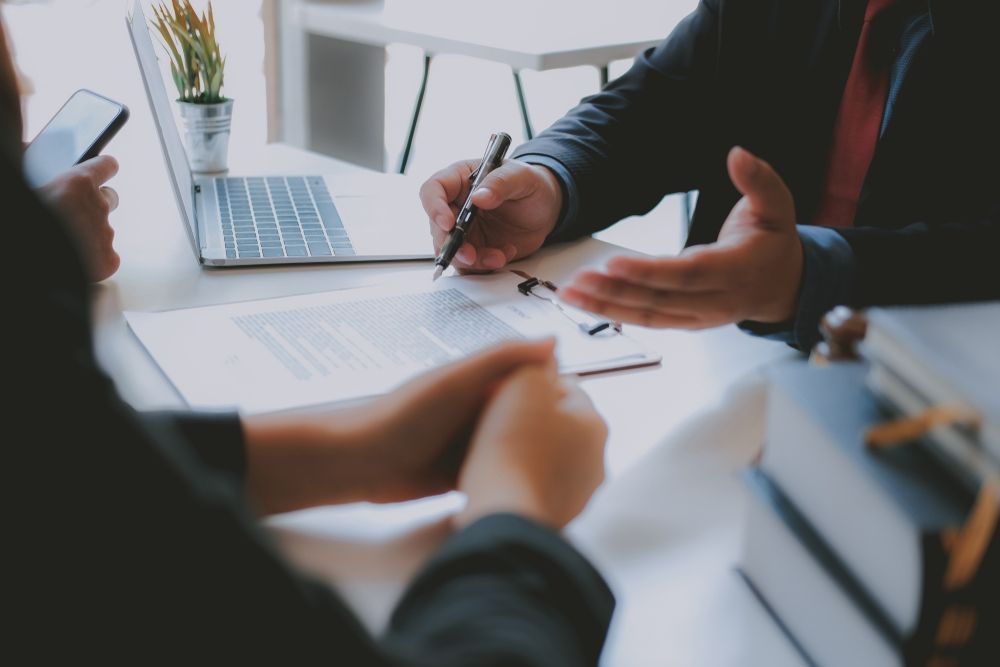 A Man And A Woman Are Sitting At A Table With A Laptop — GMS Legal & Conveyancing In 38 Canton Beach Rd, Toukley