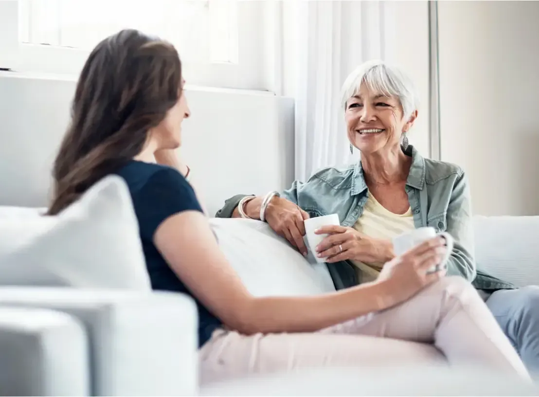 Two women sit on a white couch, drinking from mugs and talking in a living room.  GMS Legal & Conveyancing In 38 Canton Beach Rd, Toukley
