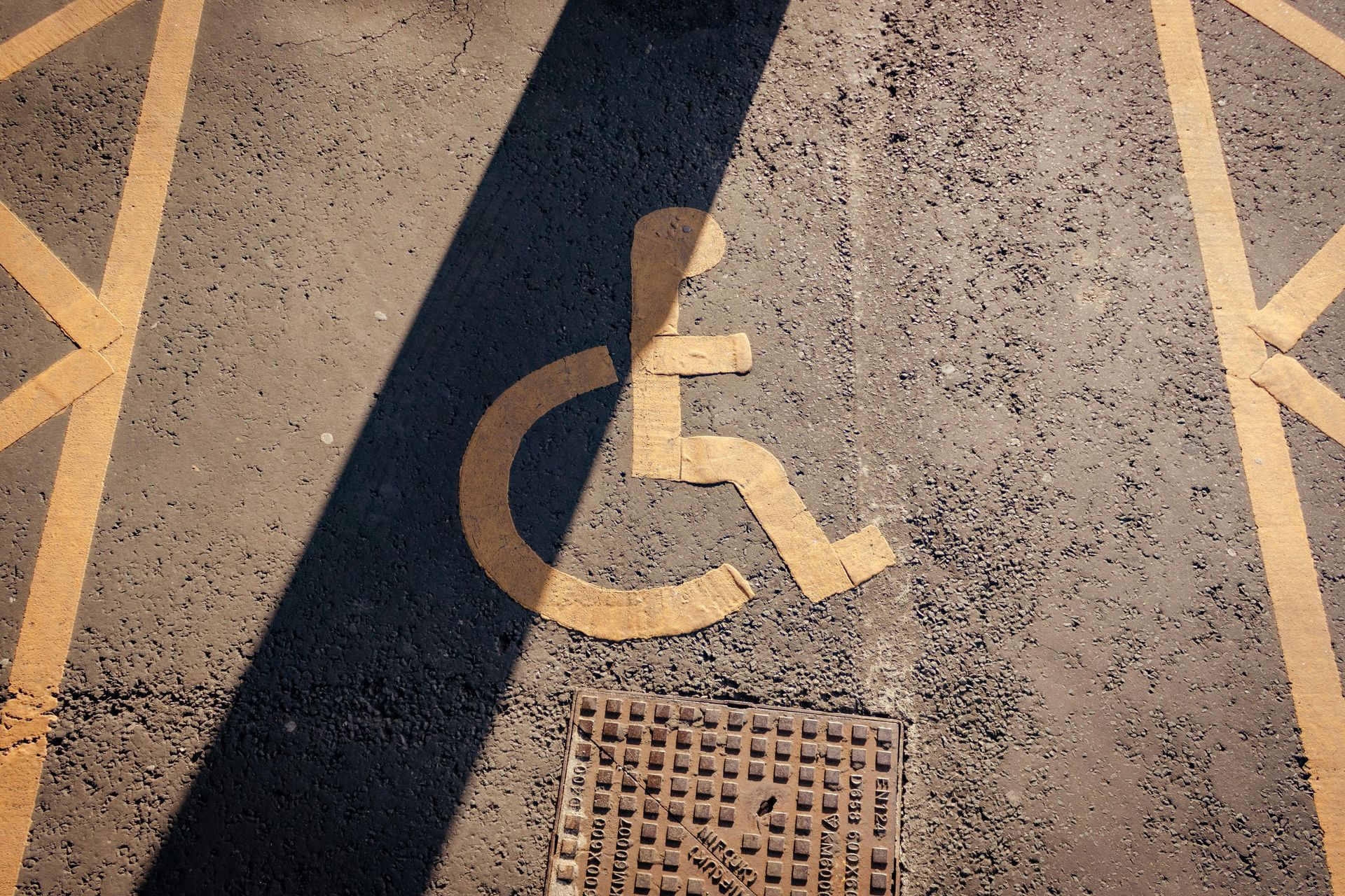 Accessible parking space with wheelchair symbol painted on asphalt near a drain cover