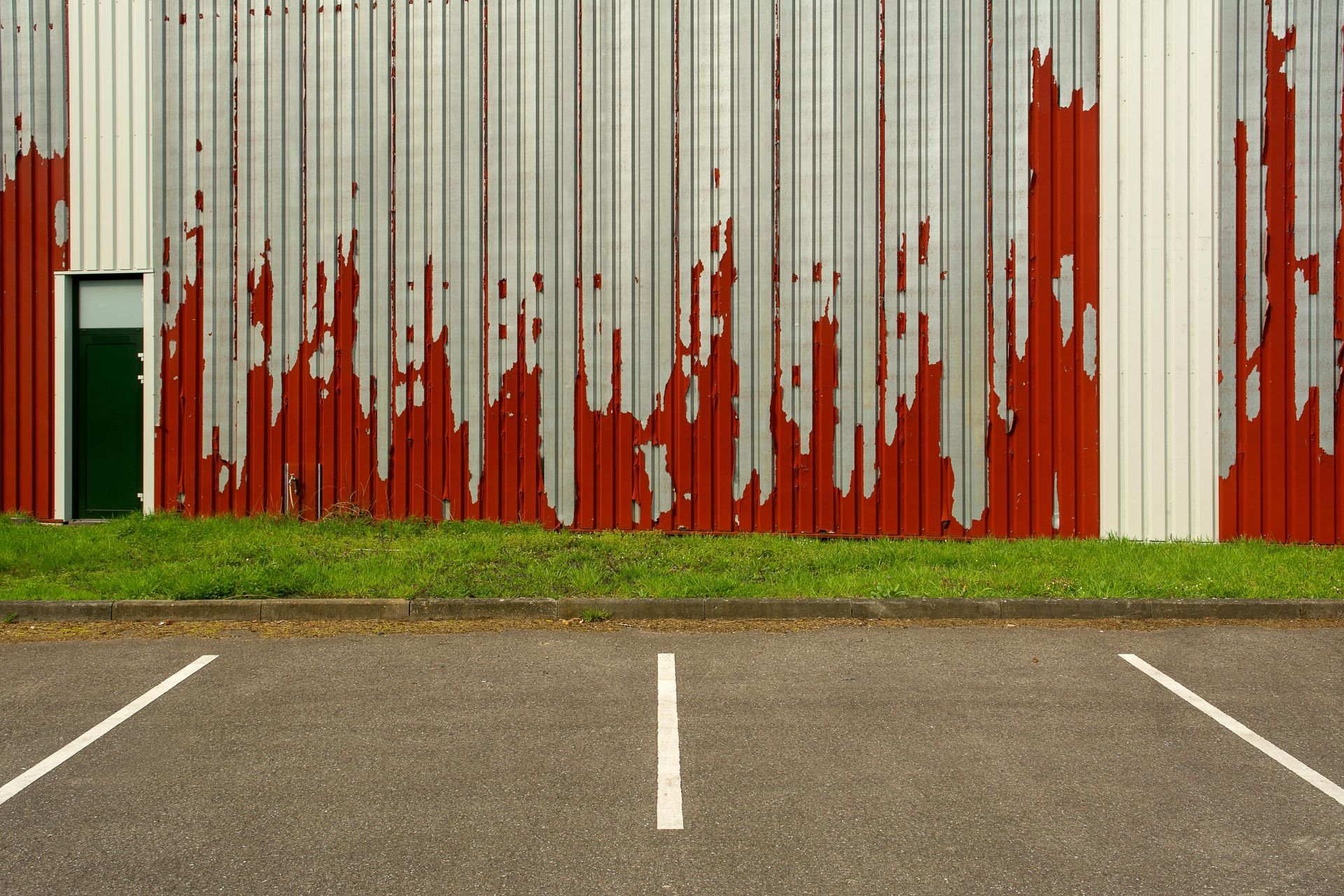 Parking lot in front of a corrugated metal wall with red paint peeling over white