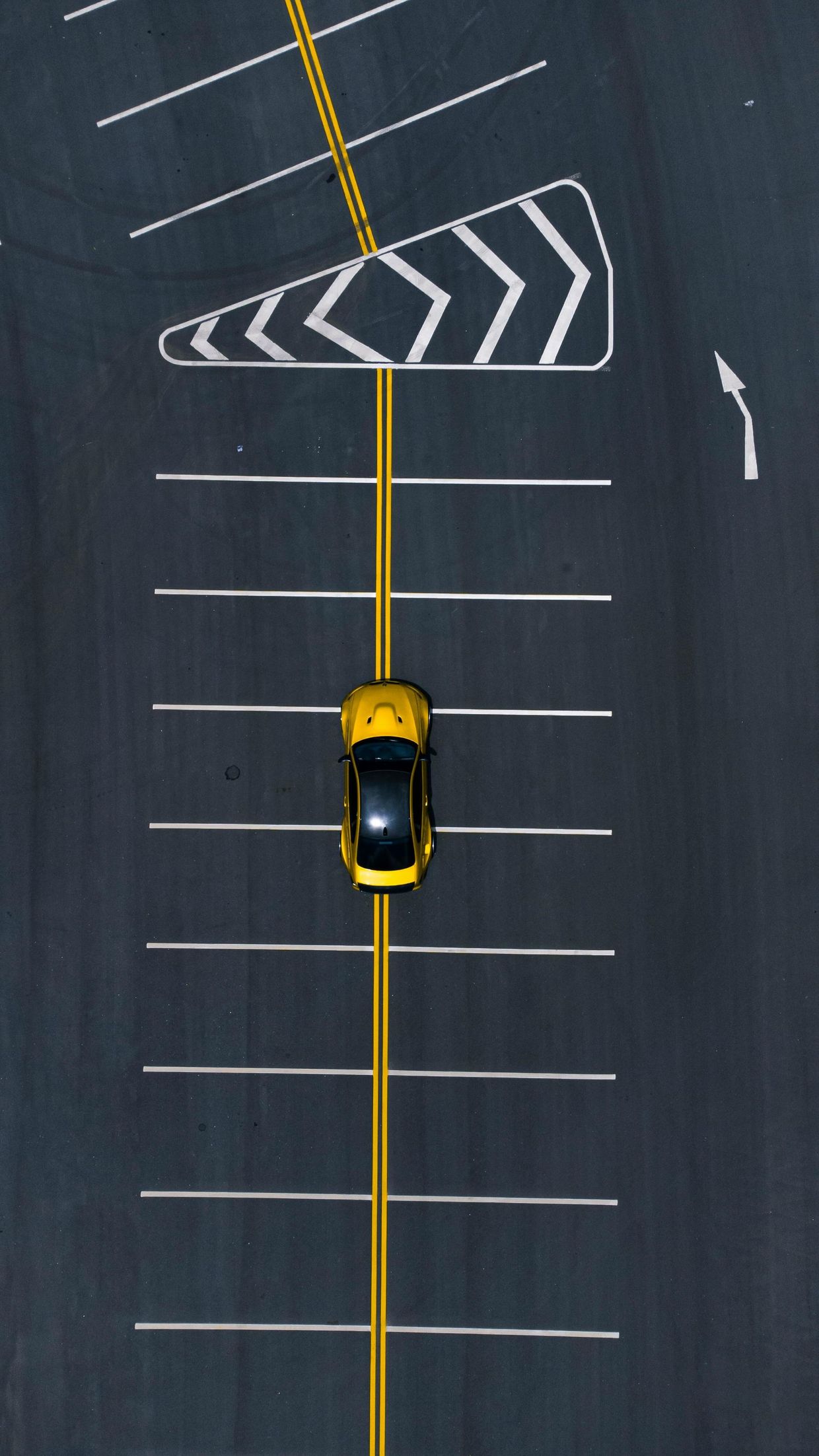 Overhead view of a yellow car centered on a marked road beside a chevron barrier ahead