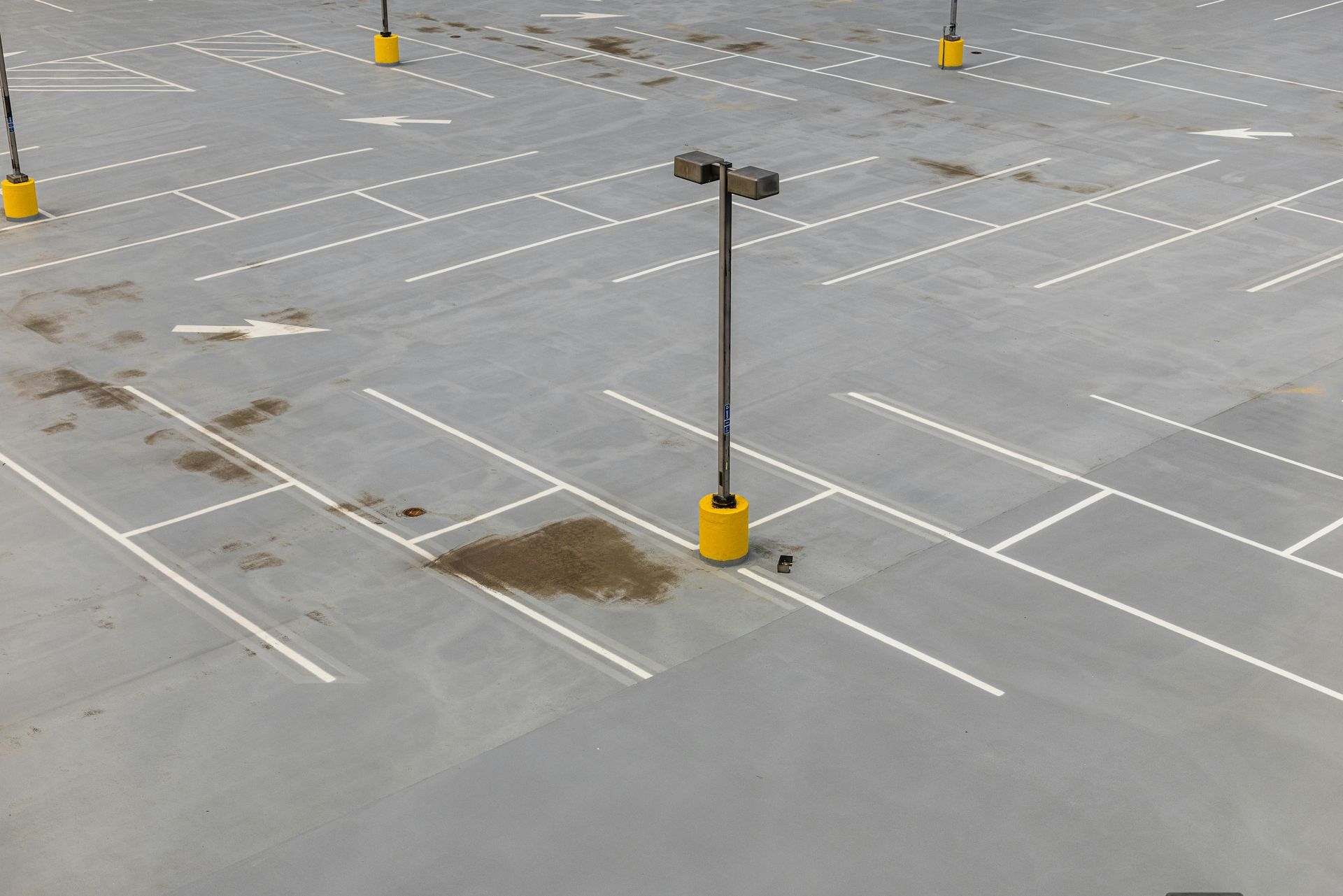 Empty parking lot with white lane markings, yellow light poles, and a few wet patches on the concrete
