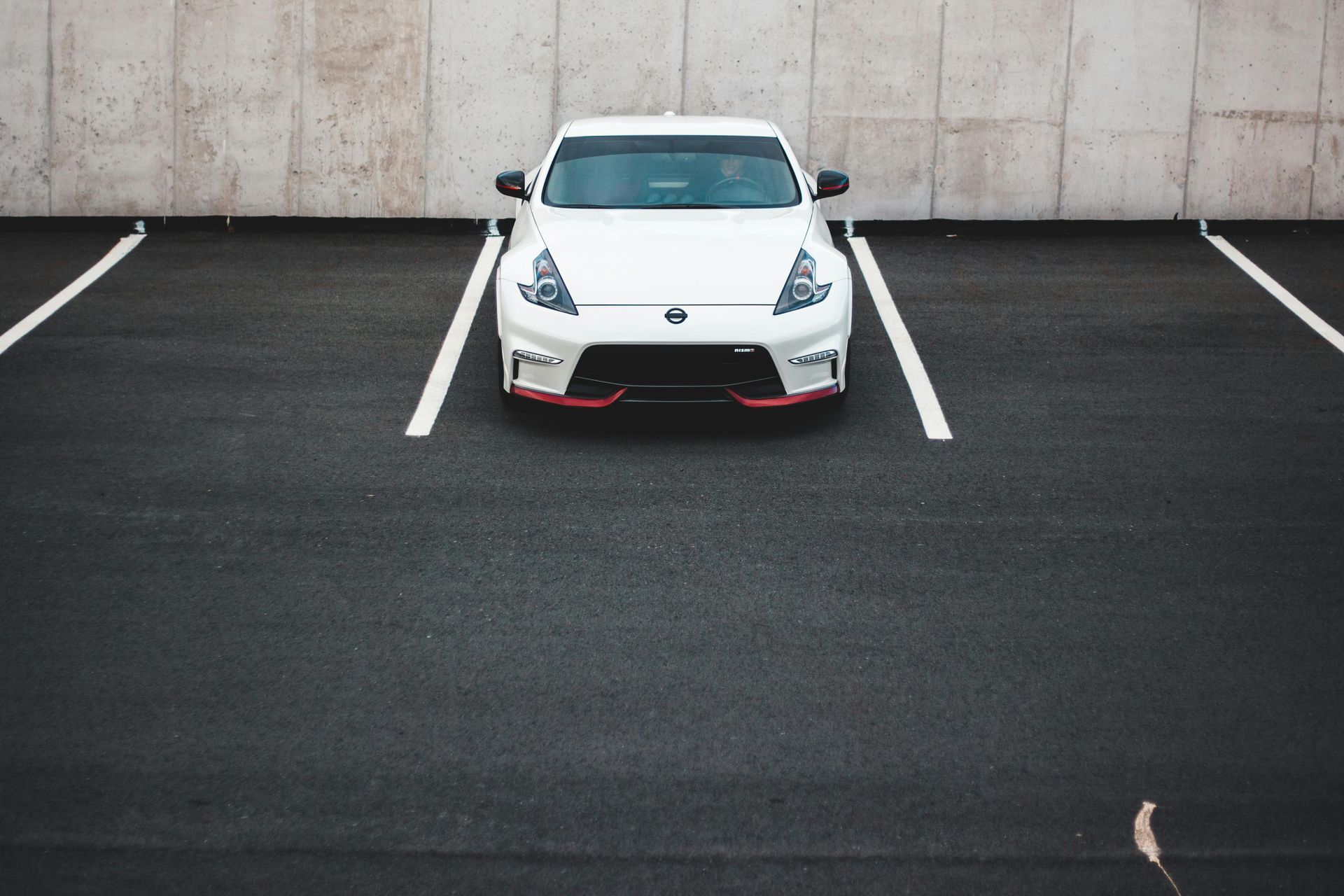 White sports car parked in a nearly empty lot with white parking lines and a concrete wall backdrop