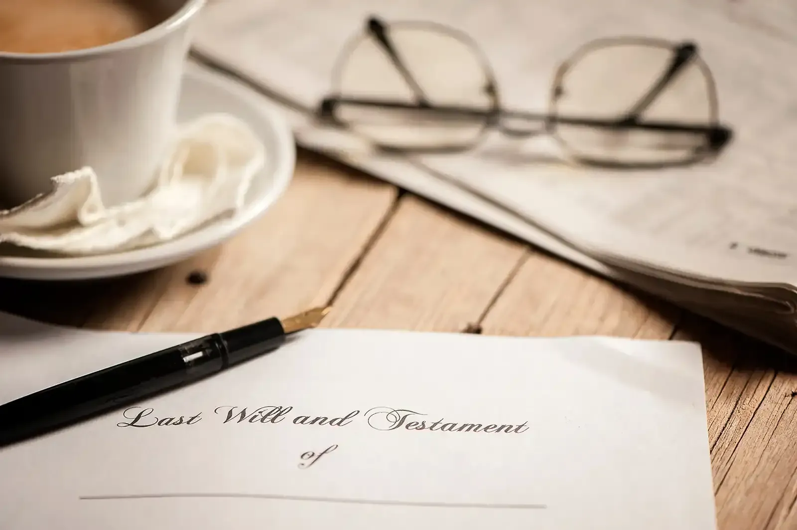 A pen is sitting on a piece of paper next to a cup of coffee and glasses, representing the topic of wills and trusts.