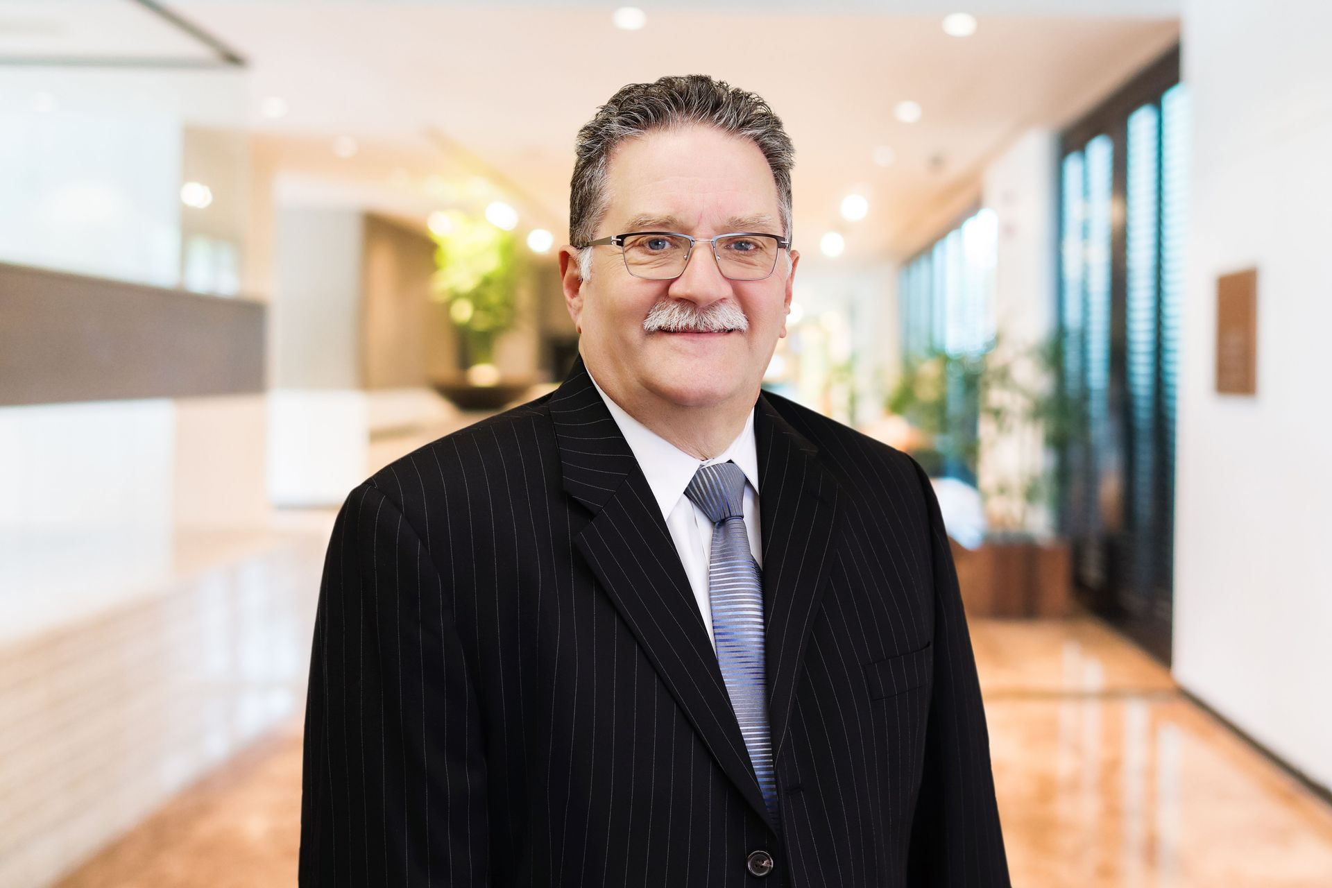 Smiling man in a dark suit standing in a bright, modern hallway