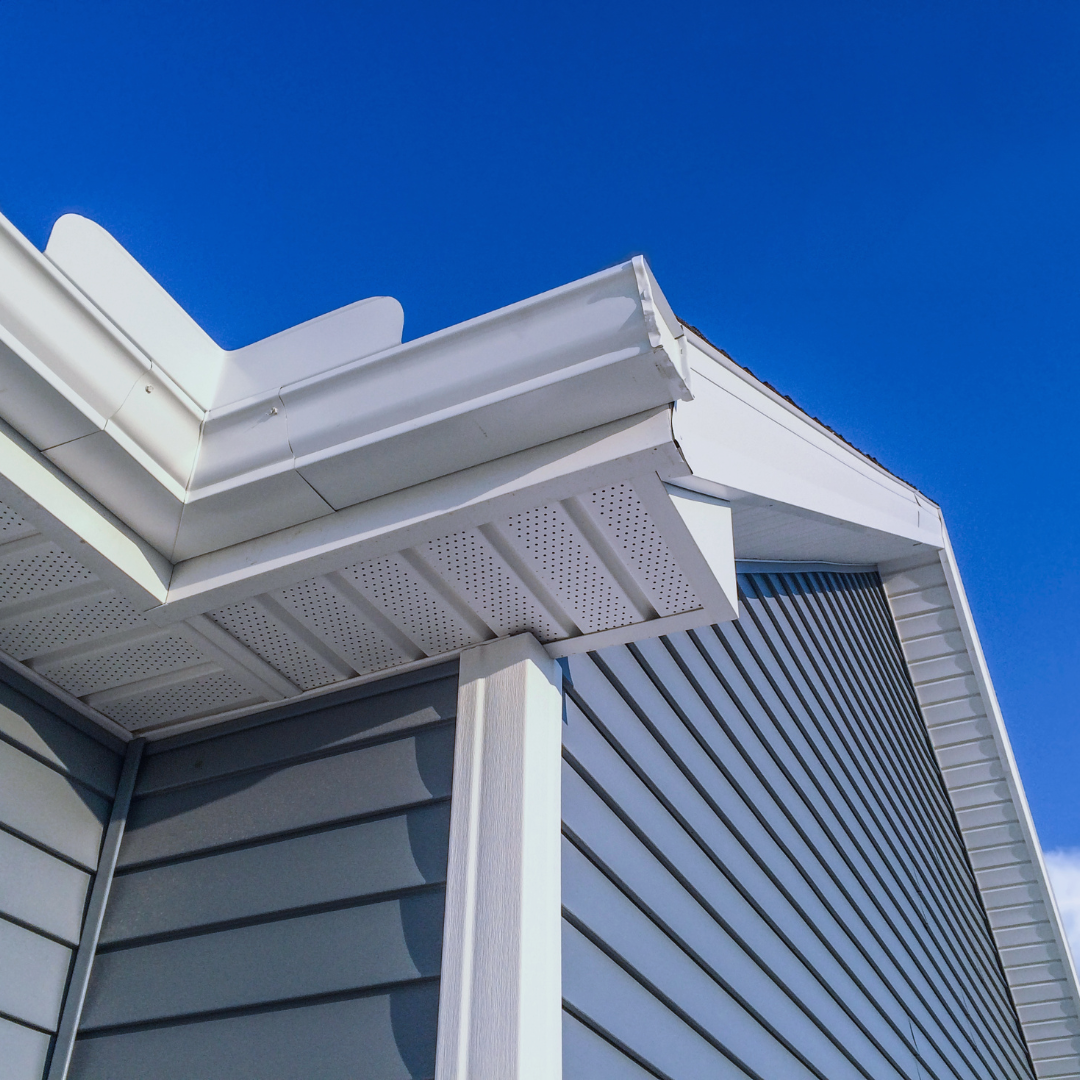 Blue siding and white trim on a building with a gutter against a bright blue sky.