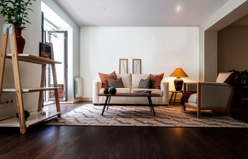 Modern living room with beige sofa, patterned rug, wooden coffee table, and warm lamp beside a chair