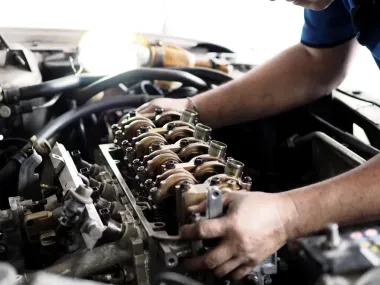 Mechanic working on exposed car engine with hands adjusting valve components