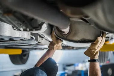 Mechanic working under a car, using both hands to inspect the underside in a garage