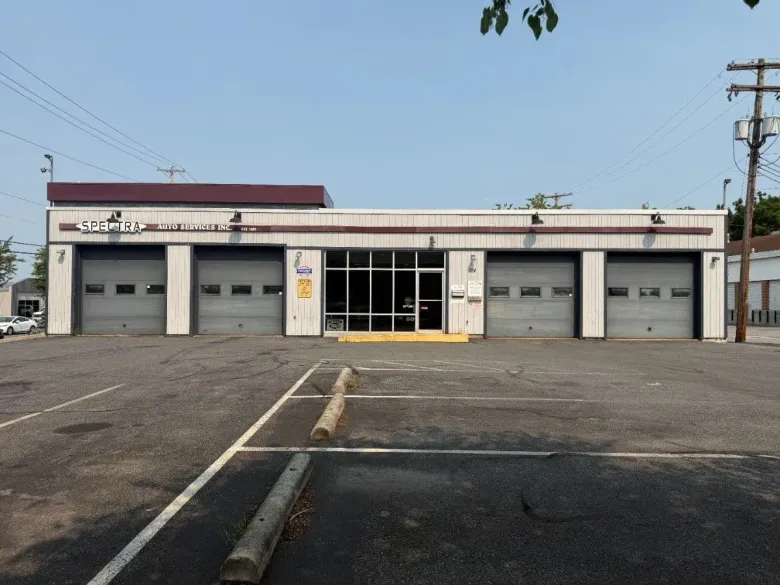 Single-story commercial building with multiple garage doors and a central glass entrance, seen from an empty lot.