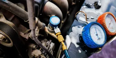 Mechanic checking car engine with pressure gauges and blue-orange hoses