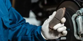 Gloved hand holding a brake pad beside a car wheel during brake repair
