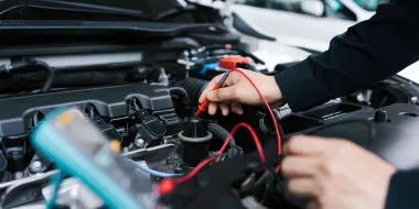 Mechanic testing a car battery with red and black cables in an open engine bay