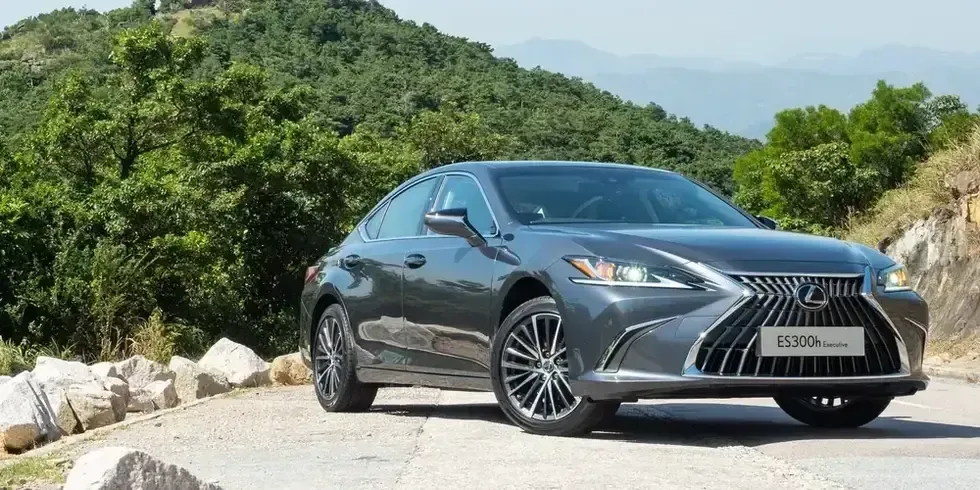 Silver sedan parked on a mountain road with green hills in the background.