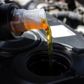 Motor oil being poured from a bottle into a car engine fill port