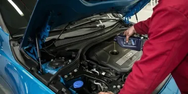 Person working under the hood of a blue car in a garage