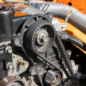 Close-up of a car engine timing belt and pulleys inside an orange engine bay