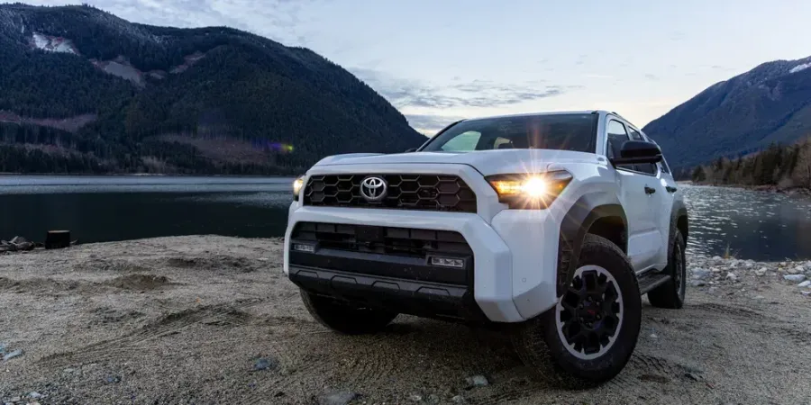White Toyota SUV parked on a rocky shore beside a mountain lake at dusk