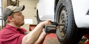 Mechanic using a cordless impact wrench to remove a car wheel lug nuts in a garage