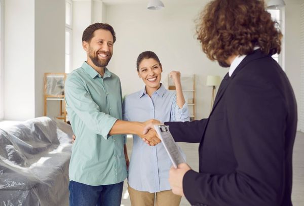 man and woman are shaking hands with a real estate agent in a living room.
