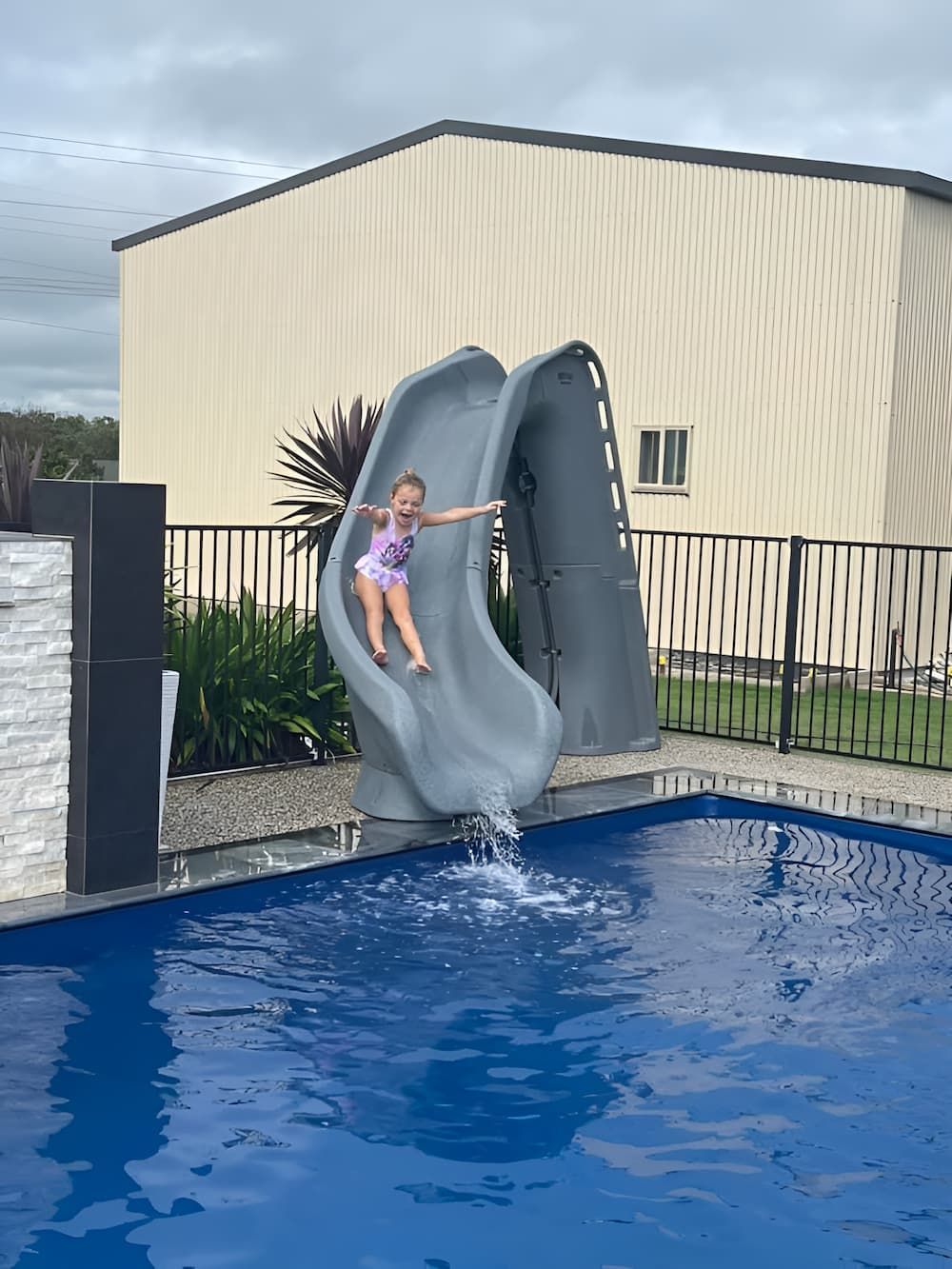 A Little Girl is Sliding Down a Water Slide Into a Swimming Pool — Aqualine Pools in Branyan, QLD