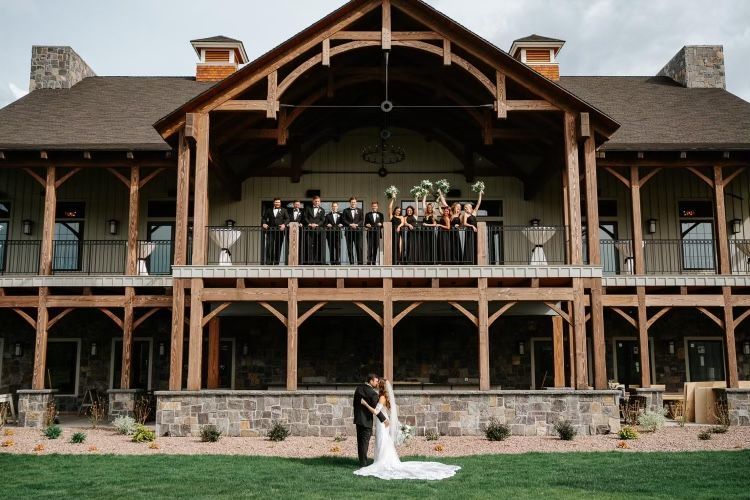 Newlyweds in formal wear in front of a lodge, wedding party on balcony.
