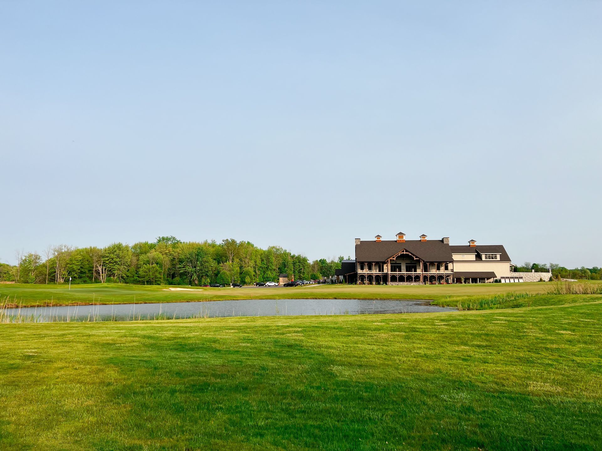 Golf course with a large clubhouse building, pond, trees, and blue sky.